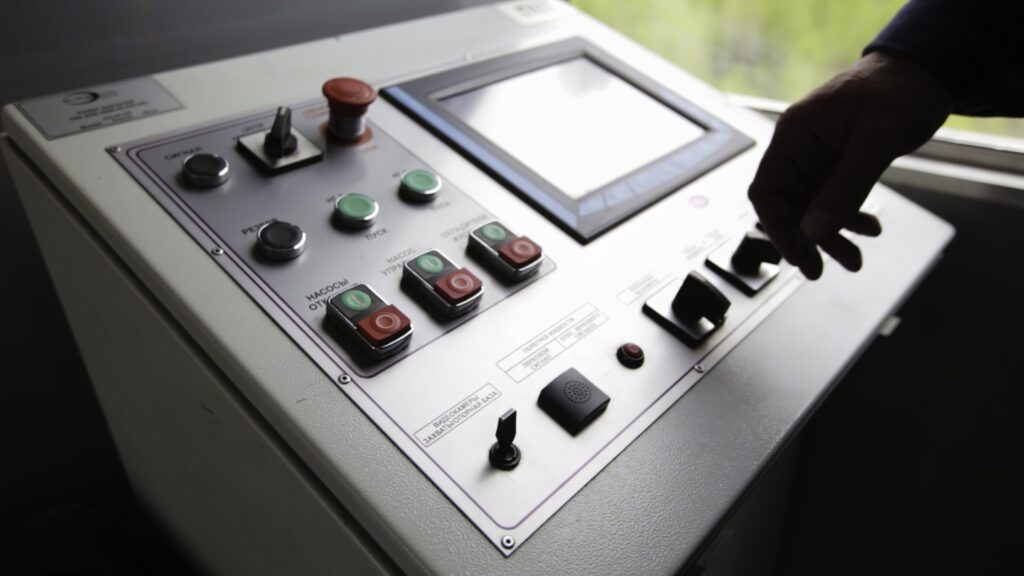 Hands operating a complex industrial control panel with various buttons and a touchscreen interface. Stock Clip