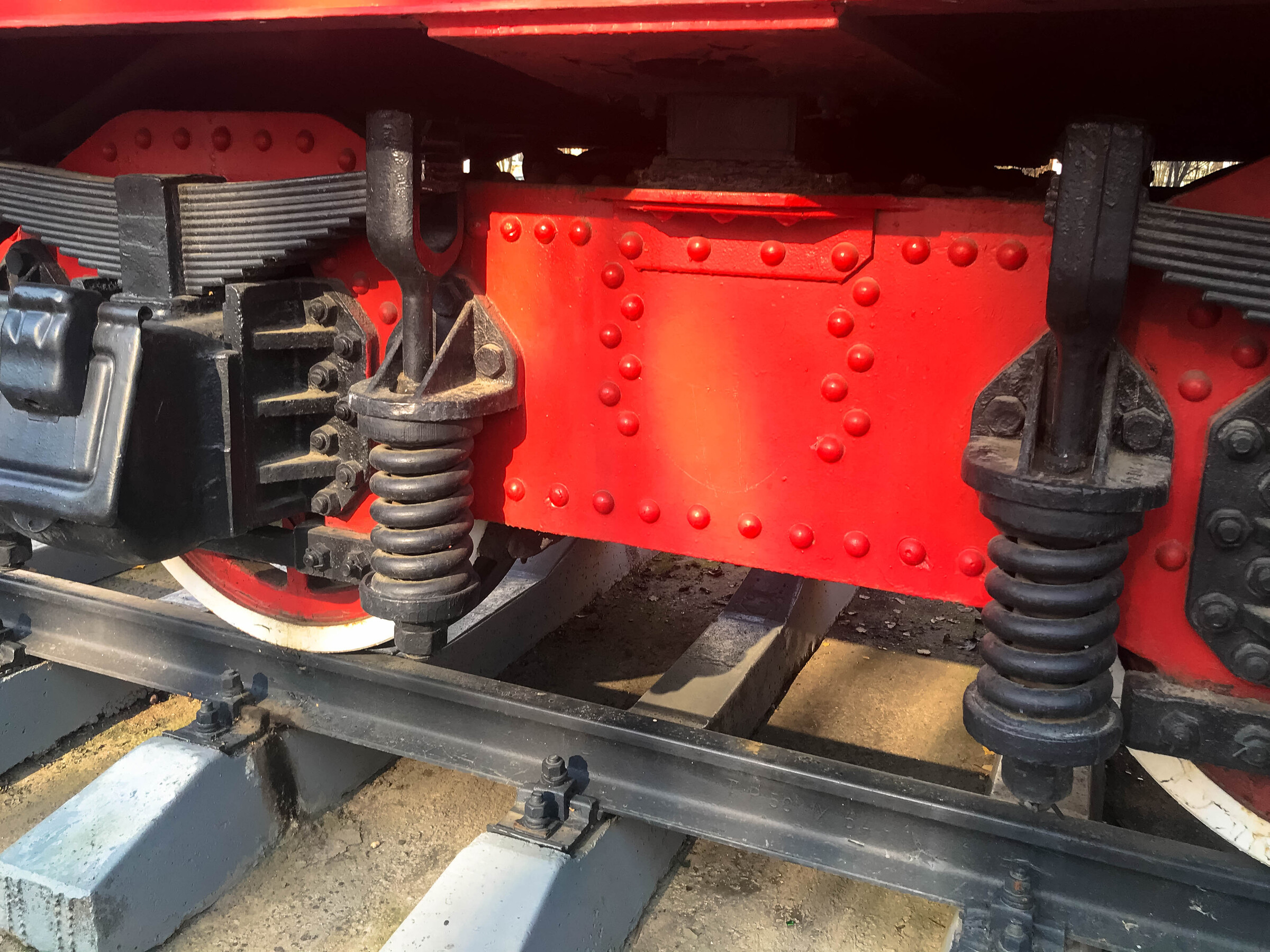 Large iron wheels of a red and black train standing on rails and suspension elements with springs of an old industrial steam locomotive.